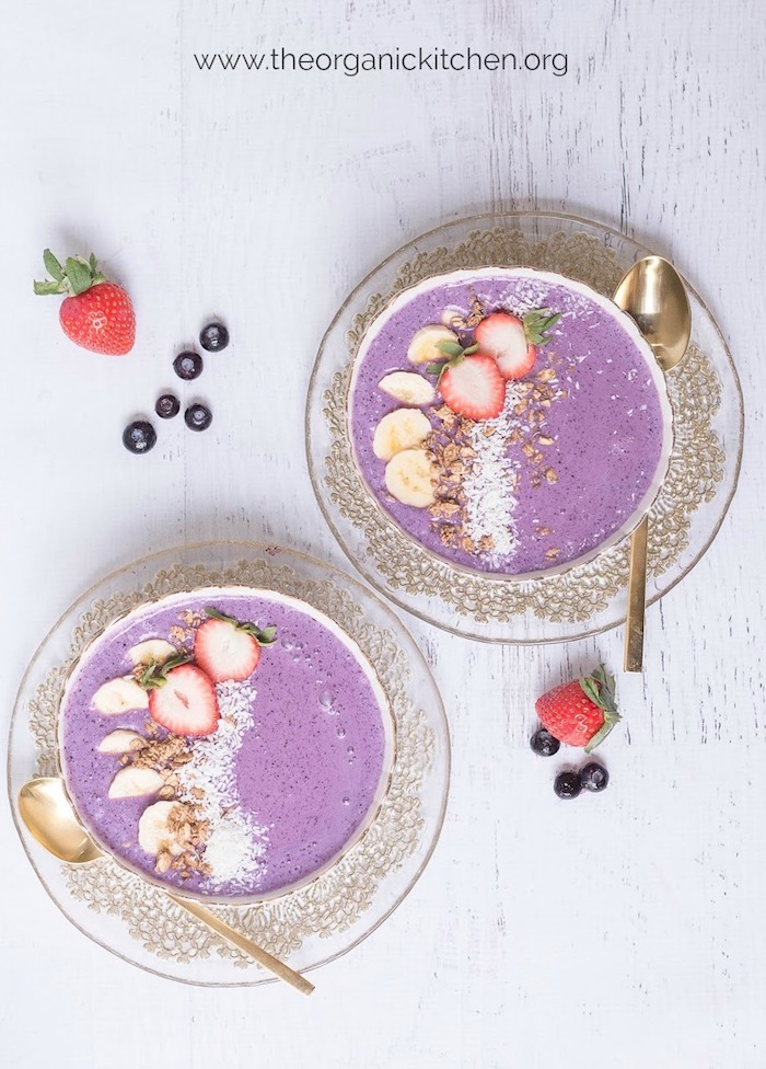Two bright purple Mixed Berry Smoothie Bowls with gold spoons set on a white wood backdrop