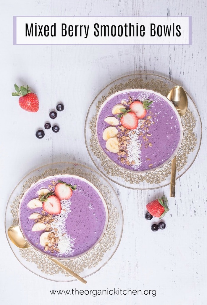 Bright Purple Mixed Berry Smoothie Bowls topped with banana slices, coconut and berries on white background
