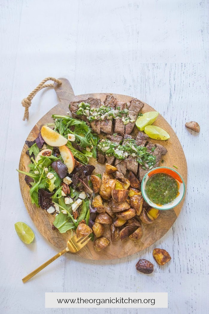 Steak with chimichurri, slad, and roasted potatoes on wooden platter