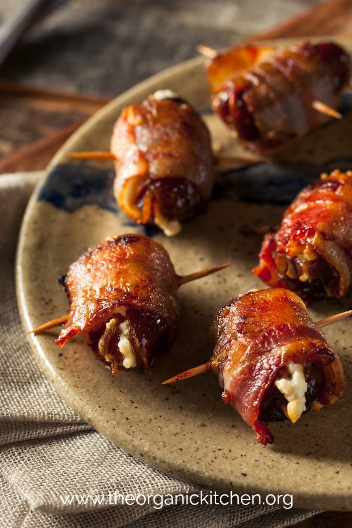 Five Goat Cheese Stuffed Bacon Wrapped Dates skewered with toothpicks on a tan plate