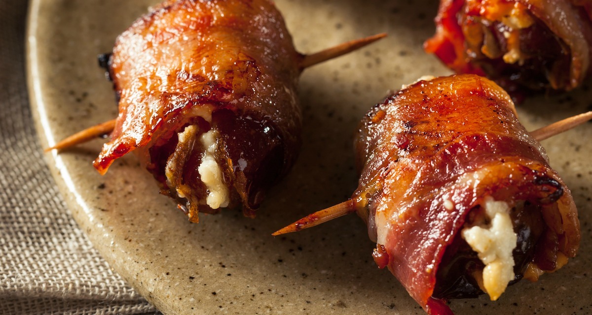 A close up of two Goat Cheese Stuffed Bacon Wrapped Dates on brown plate