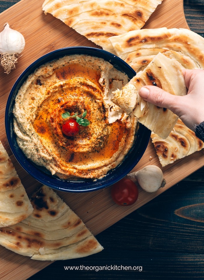 A hand holding pita after being dipped in Sun Dried Tomato Hummus!