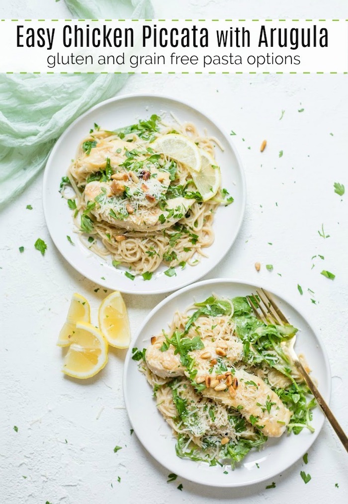 Two plates of Easy Chicken Piccata with Baby Arugula garnished with lemon wedges and parsley on a white surface