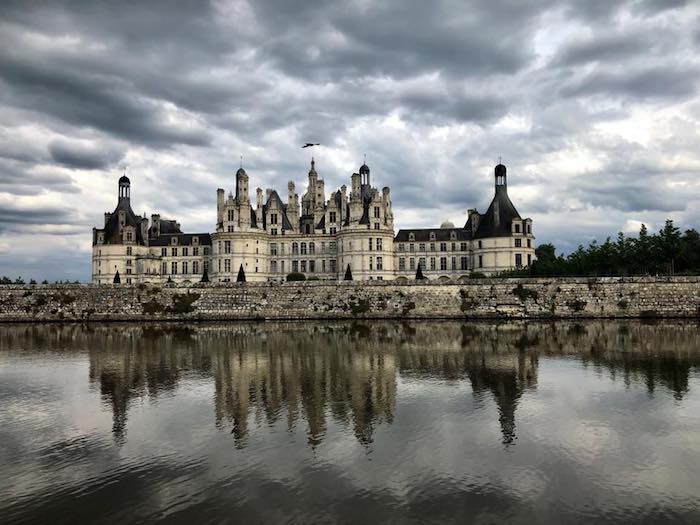 A castle in France with a lake in foreground and cloudy sky above