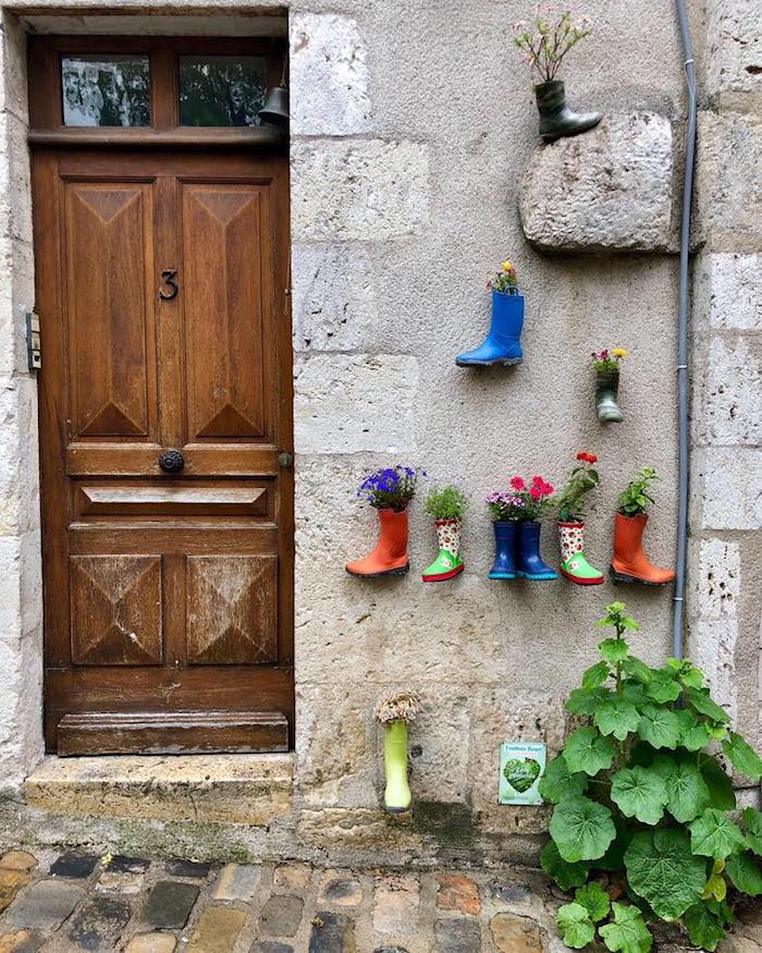 A charmingcourtyard with a wooden door and stine walls with colorful children's boots filled with flowers