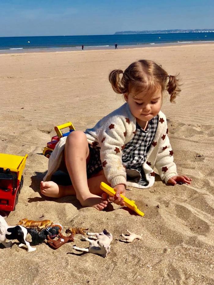 A little brunette girl playing with a yellow shovel on the beach with the ocean in the background