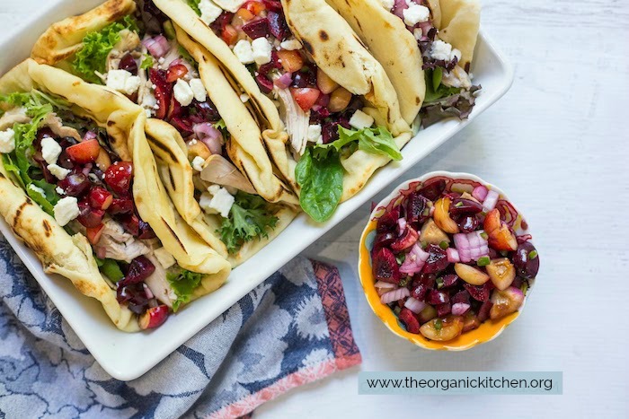 Grilled Naan Chicken Salad Wraps with Cherry Salsa in white baking dish set on blue and pink dish towel with a small, colorful bowl of cherry salsa