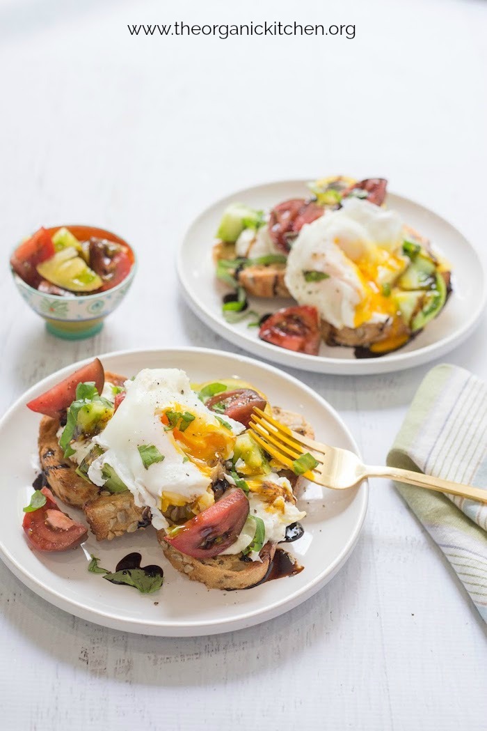 Two plates of Heirloom Tomato Burrata Toast with Poached Eggs on a white table