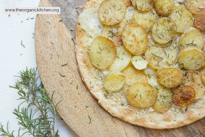 Rosemary Potato Flatbread with Cauliflower Crust Option garnished with rosemary sitting on a round wooden board