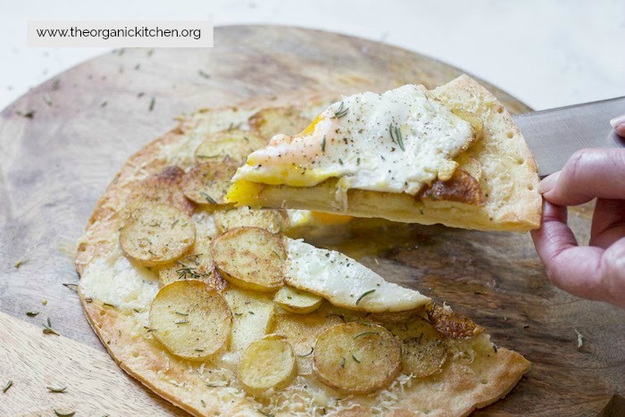 A slice of Rosemary Potato Flatbread with Cauliflower Crust Option with fried egg being lifted 
