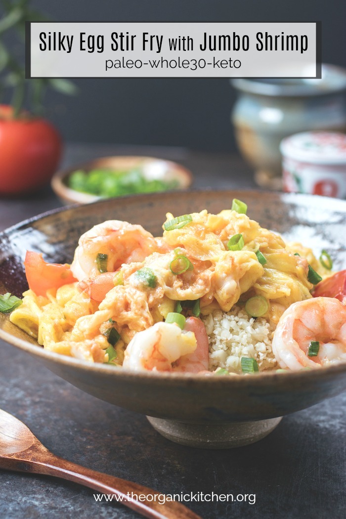 Silky Egg Stir Fry with Jumbo Shrimp in a gray bowl with tomatoes, onions and decorative jars in the background