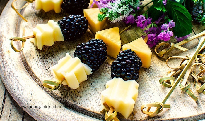 Cheese and blackberries on skewers surrounded by greens and purple flowers