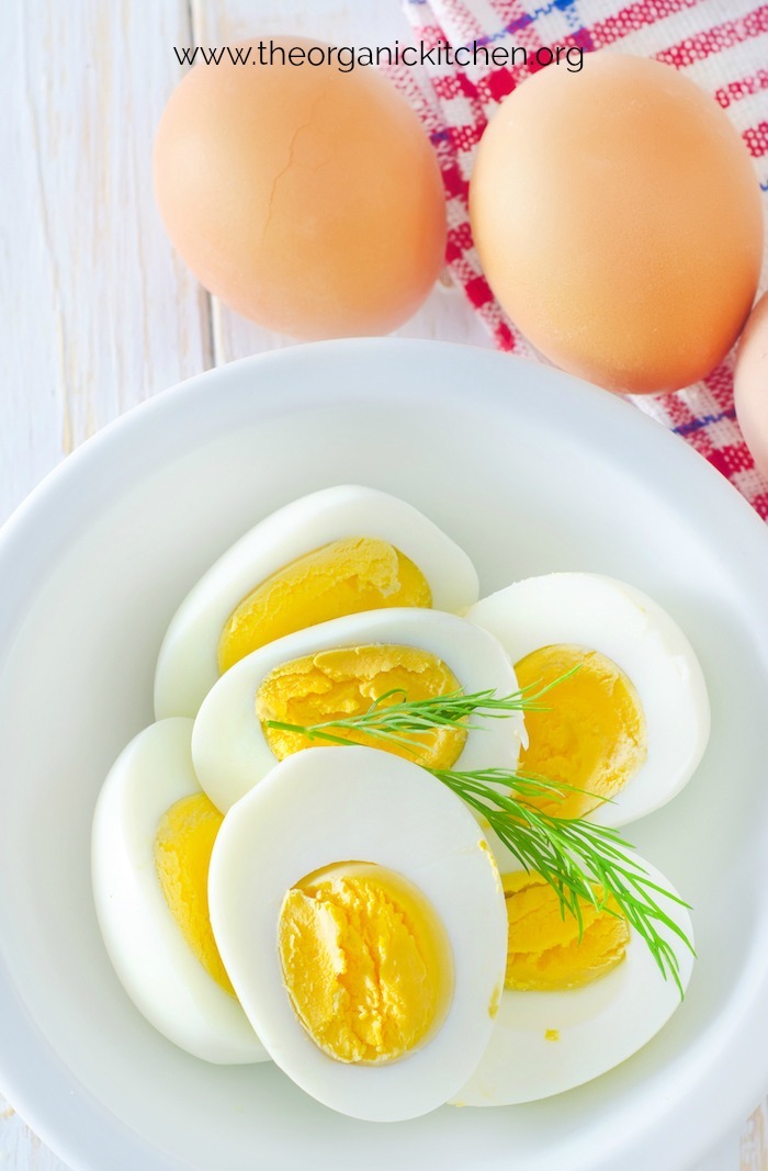 Hard boiled eggs in a white bowl with red and white dish towel in the background
