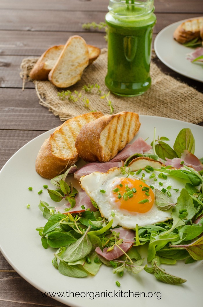 Simple Green Salad with Ham and Fried Egg on white plate with green juice and bread in background