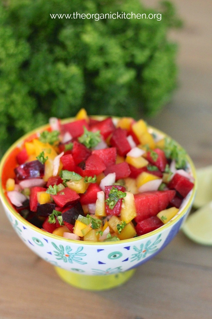 A small bowl of plum salsa on a wood table with lime wedges and cilantro
