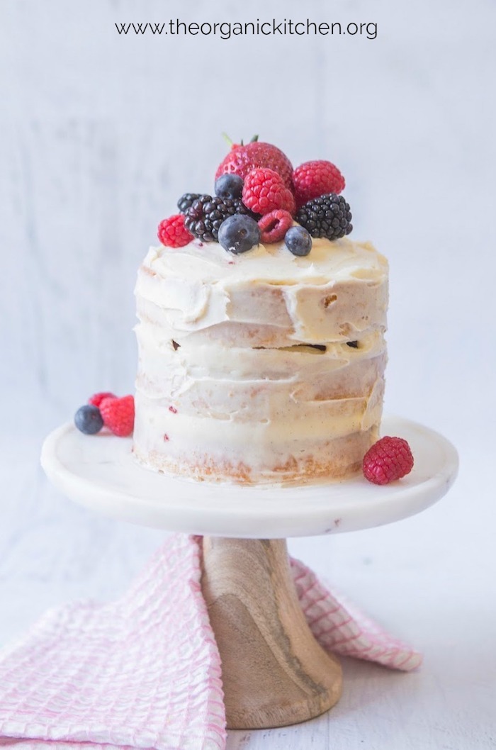 Mini Vanilla Cake with Buttercream and Berries on a small marble and wood cake stand