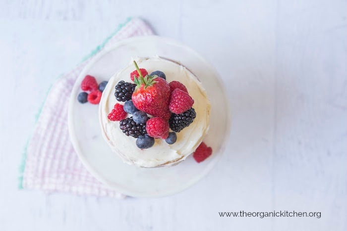 A tiny white cake topped with colorful berries  on a white cake plate