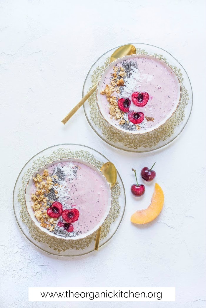Two Peach Cherry Smoothie Bowls on gold laced plates with gold spoons