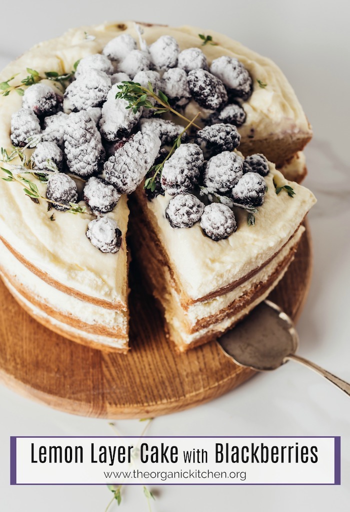 Lemon Layer Cake with Blackberries on a round wooden board with silver serving utencil