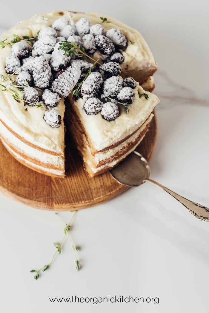 Triple layer Lemon Layer Cake with Blackberries on wooden cake plate with silver serving spatula