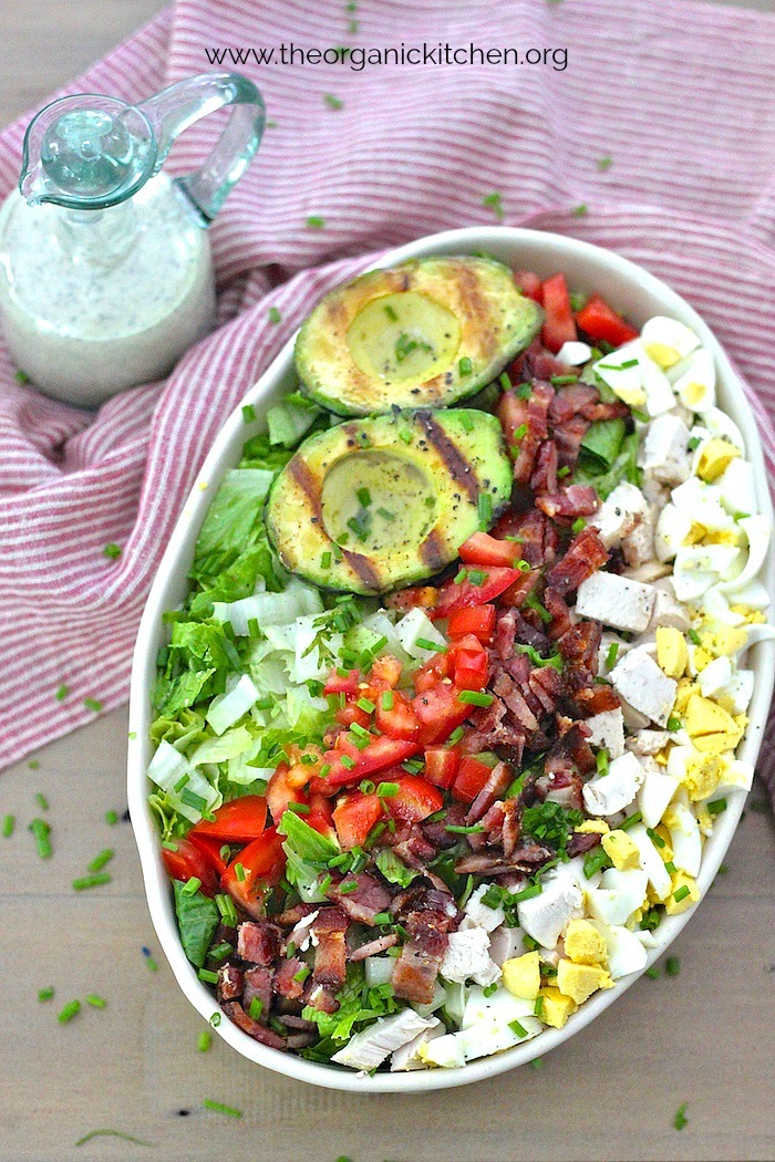 Grilled Avocado Cobb Salad (Keto-Paleo-Whole30) in a white dish with a bottle of ranch dressing set on a white and red dish towel