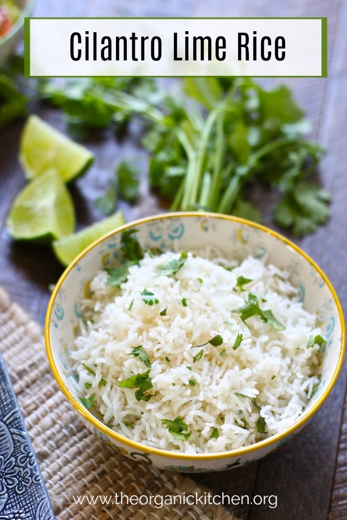 Cilantro Lime Rice in a bowl on wood table surrounded by herbs and lime wedges