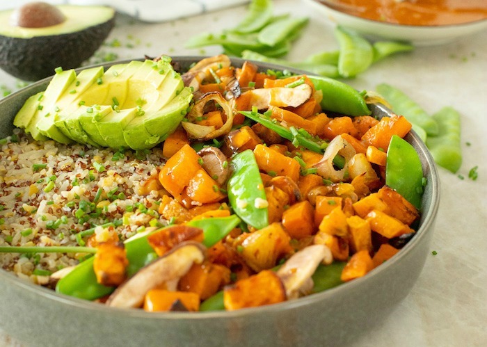 Sliced avocado on top of grains and vegetables in a gray bowl