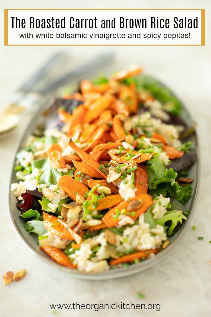 Roasted Carrot and Brown Rice Salad on a gray platter with serving spoons in the background