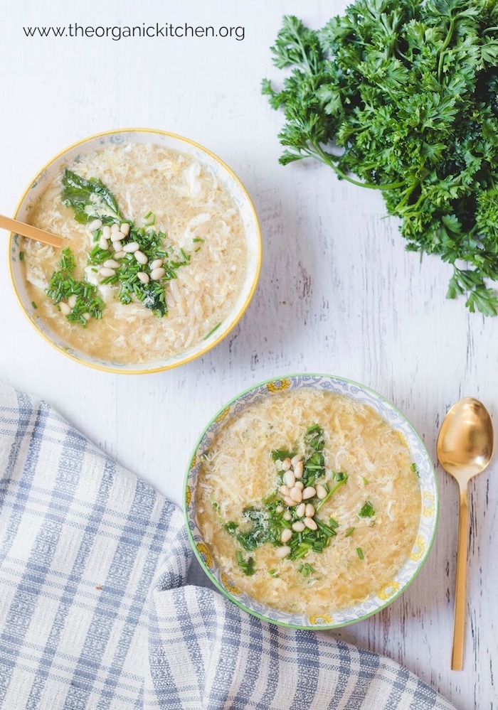 Two bowls of Italian Egg Drop Soup on white table with gold spoon