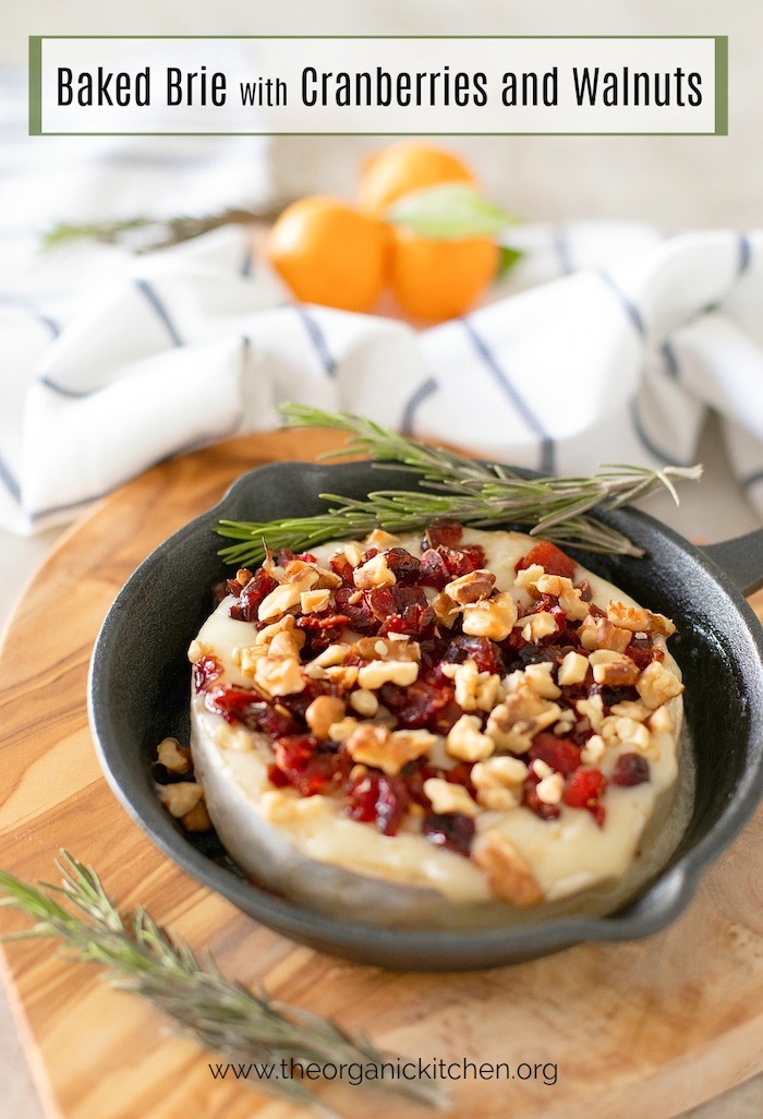 Baked Brie Appetizer with Cranberries and Walnuts in a small cast iron skillet set on wooden serving board