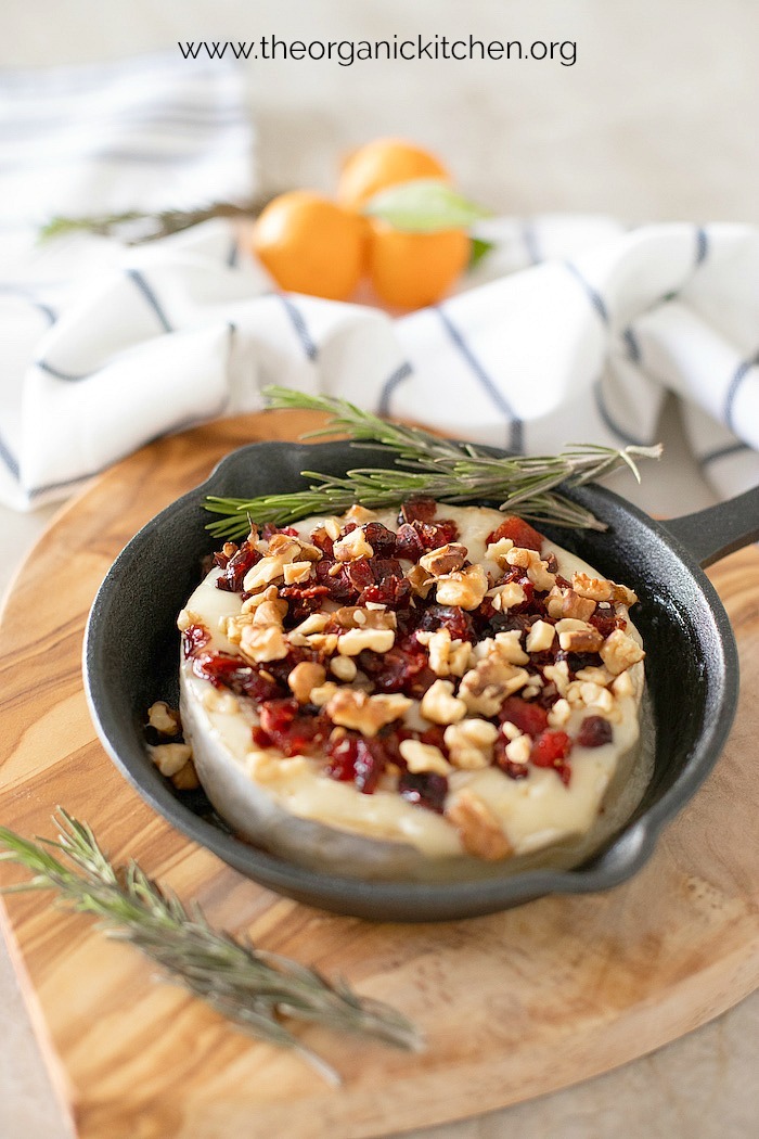 Baked Brie Appetizer with Cranberries and Walnuts in a small black pan with dish cloth and oranges in the background