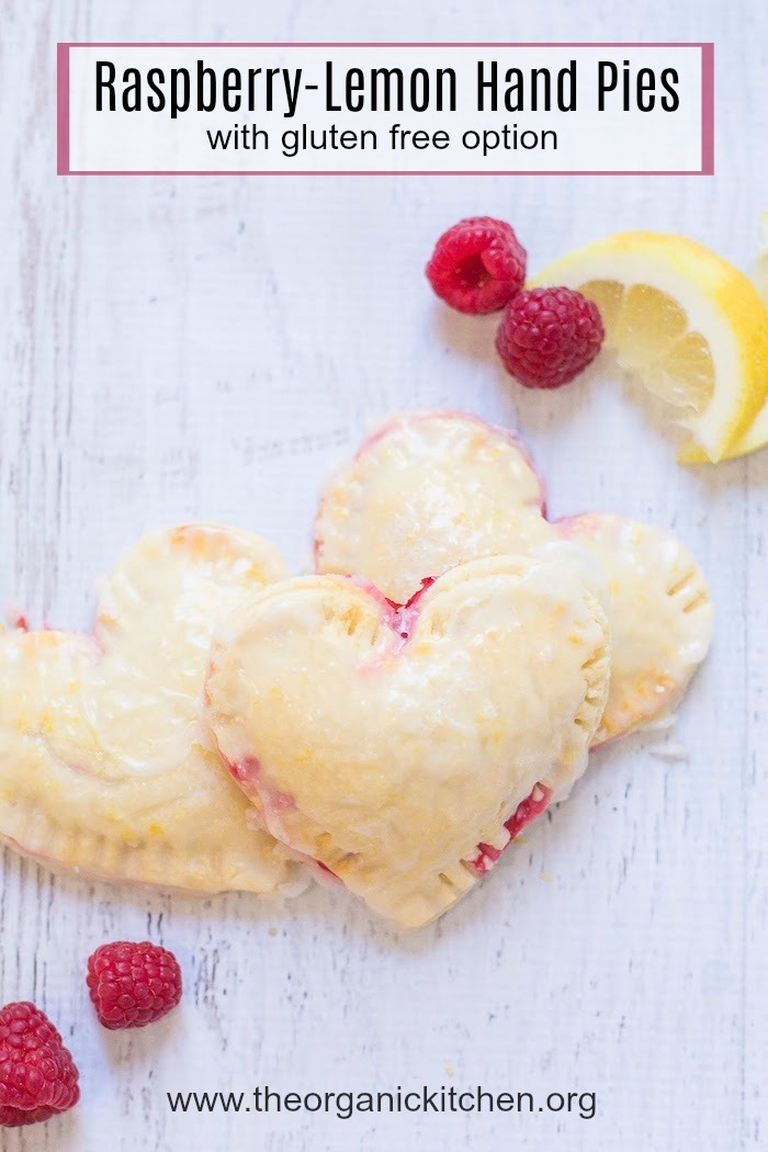 Heart shaped Raspberry-Lemon Hand Pies surrounded by raspberries and lemon slices on white background