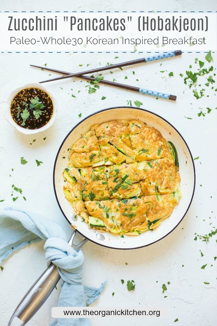 Zucchini Pancakes (Hobakjeon) in a white pan on a white surface, surrounded by a bowl of sauce, chopsticks, and blue cloth