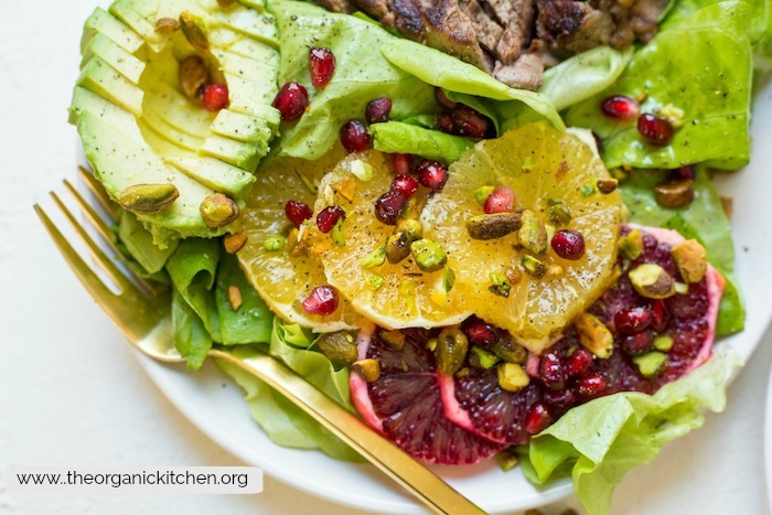 Steak with Citrus and Avocado Salad garnished with pomegranate seeds on white plate with gold fork