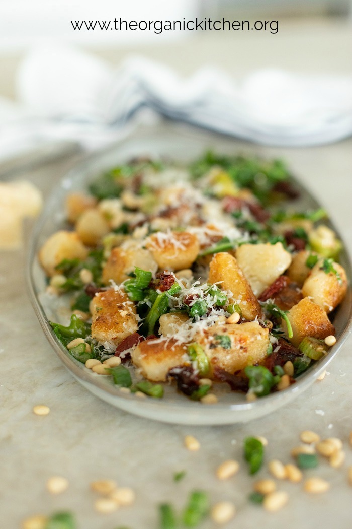 A gary platter of Gnocchi with Sun Dried Tomatoes and Baby Arugula garnished with chives and parmesan cheese