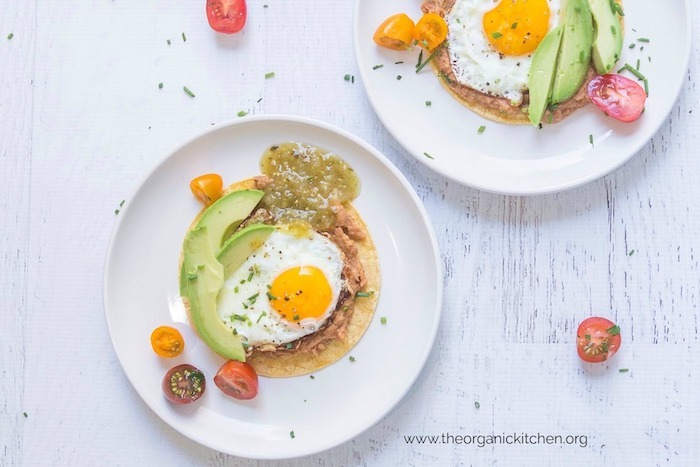 Fried eggs with beans and avocado on tortillas set on white plates