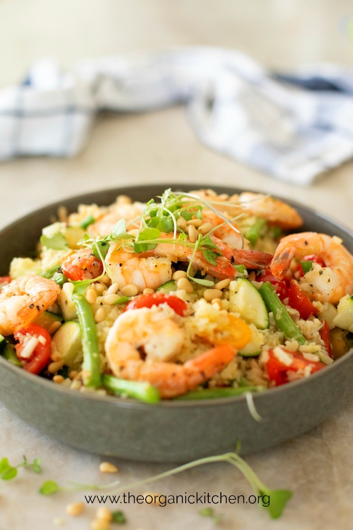 Lemony Shrimp and Vegetable Stir Fry Bowl garnished with pine nuts and micro-greens on marble surface with blue and white towel in background