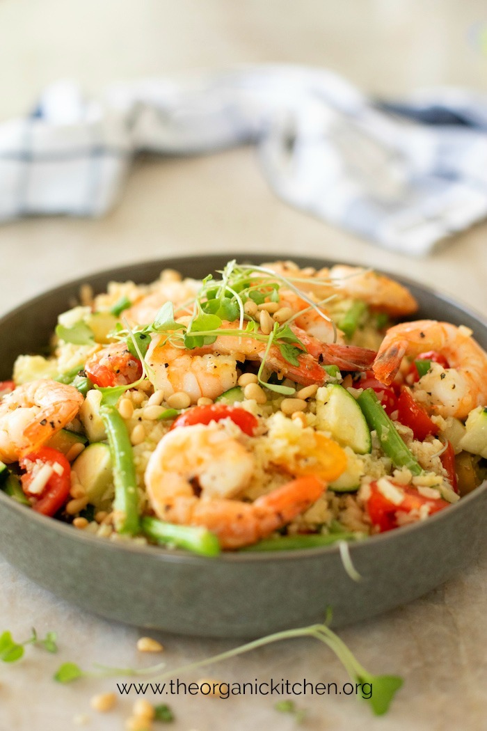 Lemony Shrimp and Vegetable Stir Fry Bowl garnished with pine nuts and micro-greens on marble surface with blue and white towel in background