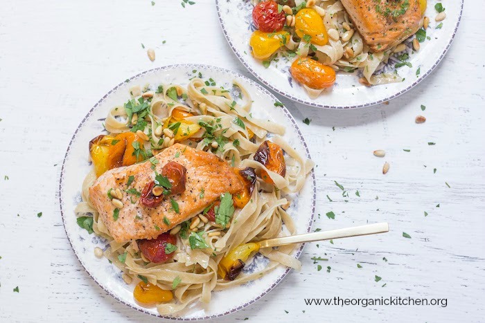 Two plates filled with Crispy Salmon with Blistered Tomatoes and Pasta with gold fork