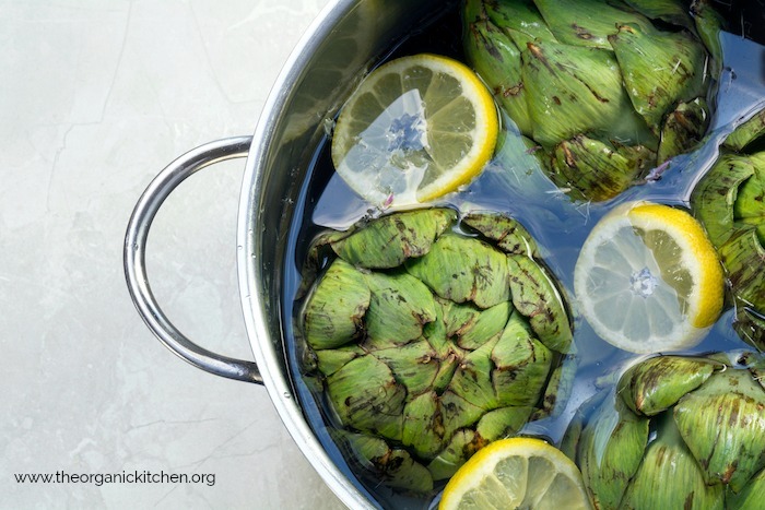 Artichokes and lemon wedges in a stock pot filled with water