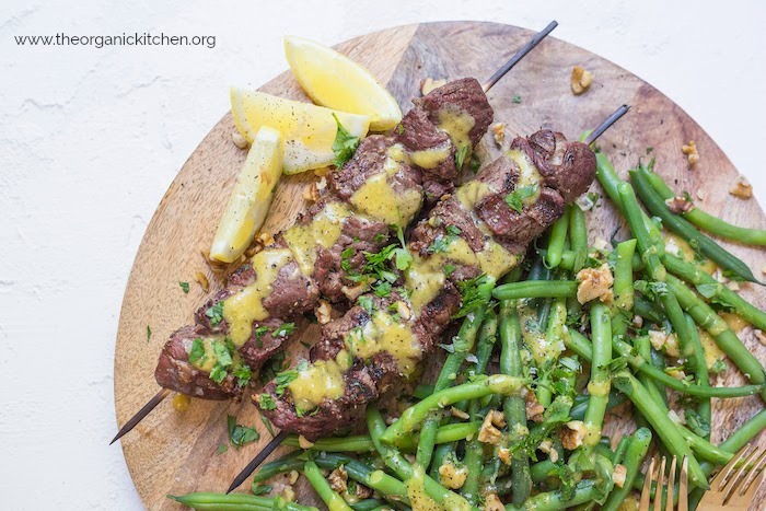 Steak Kabobs with Dijon Green Beans on wood platter garnished with lemon wedges