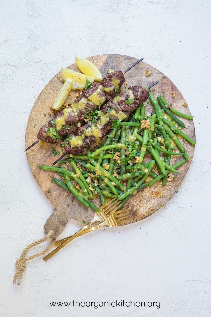 Steak Kabobs with Dijon Green Beans with lemon wedges served on a wood platter