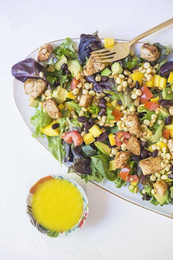 A vertical photo showing Southwest Chicken Salad with Mango Vinaigrette on a light blue platter with a colorful small bowl of bright yellow salad dressing