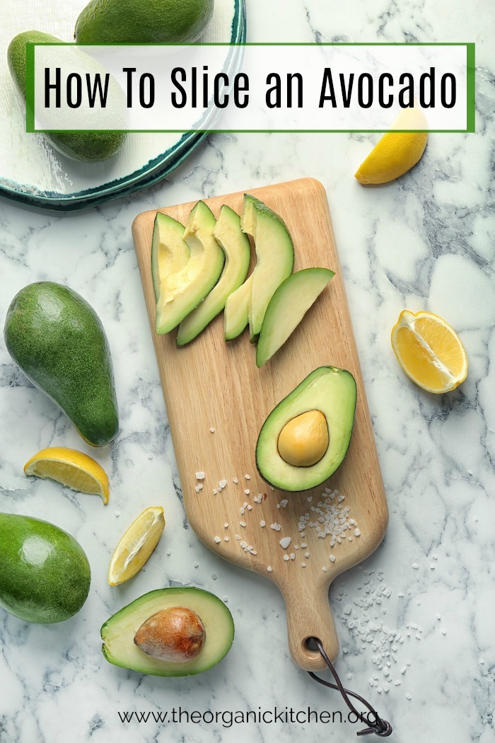 How to slice an avocado: A marble surface with a cutting board with half and avocado and avocado slices on it, surrounded by avocados and oranges