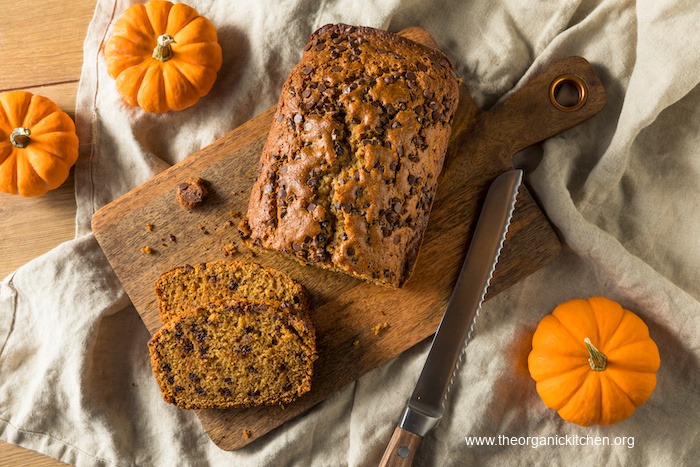 Homemade Chocolate Chip Pumpkin Bread on wood serving board surrounded by baby pumpkins