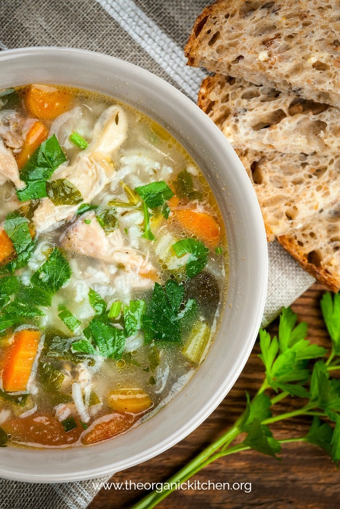 Chicken and rice soup with vegetables in bowl and bread from above with bread and parsley on wood table