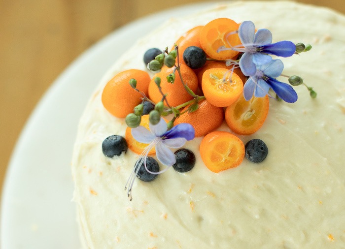 A close up of Orange Blueberry Cake topped with kumquats, blueberries and flowers