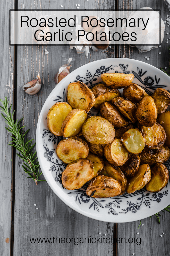 Whole30 Roasted Potatoes (with Rosemary Garlic Option) in a black and white bowl on gray wood surface surrounded by rosemary springs and garlic