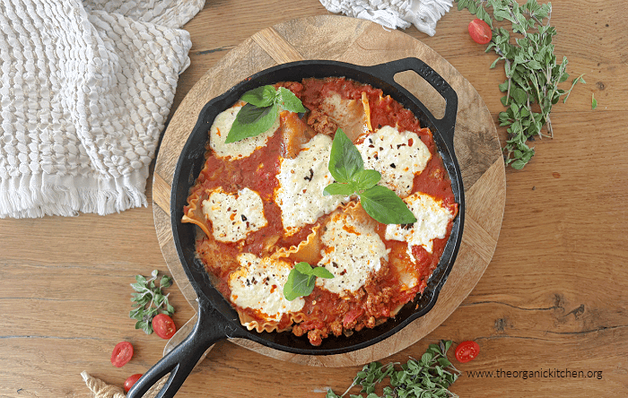 Stove Top Skillet Lasagna in a black cast iron pan surrounded by herbs and cherry tomatoes