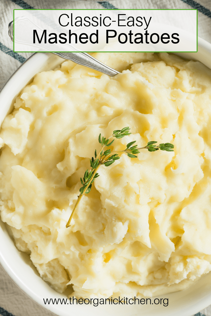 Classic Easy Mashed Potatoes garnished with thyme in a white bowl with silver spoon